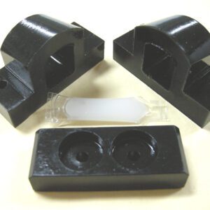 Black plastic parts and a white cylindrical piece on a white surface.
