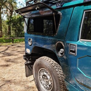 Blue off-road vehicle parked on a dirt path in a wooded area.